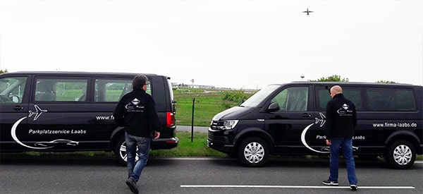 Shuttlebusse vor dem Flughafen Berlin BER - Mitarbeiter laufen zu den Bussen, im Hintergrund startet ein Flugzeug